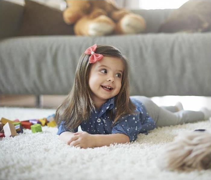 young girl laying on carpeted floor; toy blocks beside her